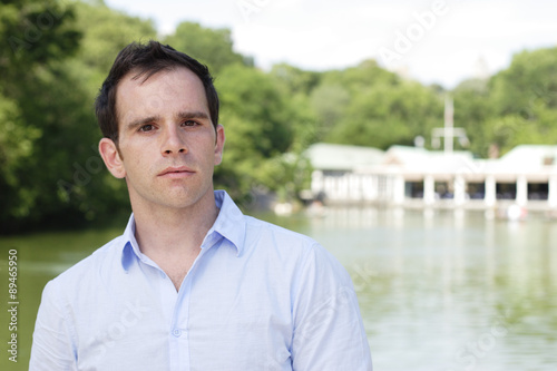 Fotografie, Obraz Man standing in front of lake and boathouse looking at camera.