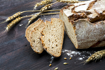 rustic loaf of bread and slices with wheat on dark wood