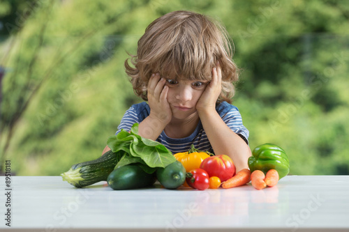 Fotografia Cute little boy sitting at the table, unhappy with his vegetable meal, bad eatin