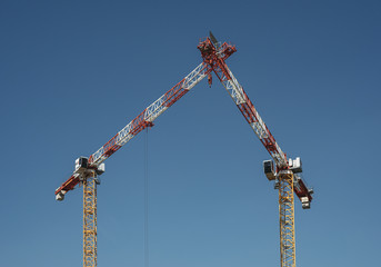 Two construction cranes meeting against a blue sky