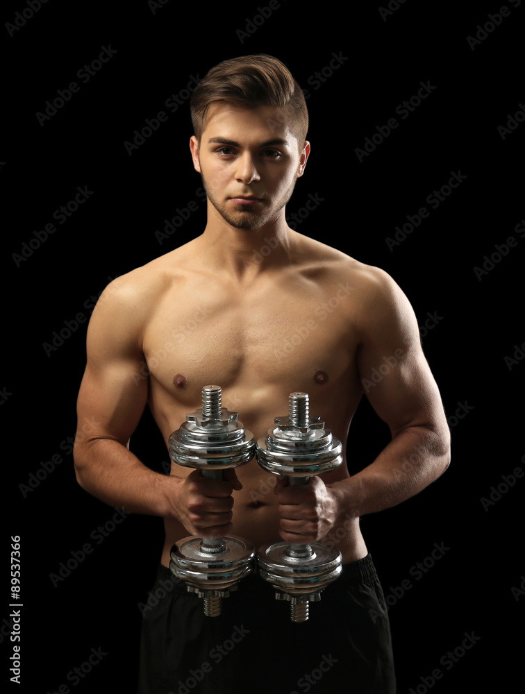 Muscle young man holding dumbbells on dark background
