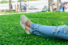 Cropped Woman Legs In Denim With White Sneakers Resting On Grass