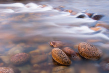 Pebbles In Shallow Fast-flowing Stream, Photographed With Slow Shutter Speed To Blur Motion.