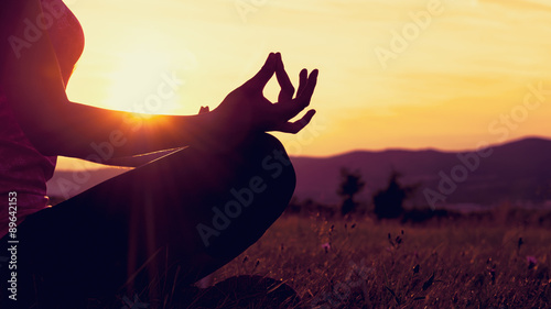 Fotomural Young athletic woman practicing yoga on a meadow at sunset, silhouette