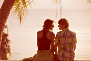 Young couple sit together under a palm tree and looking toward s