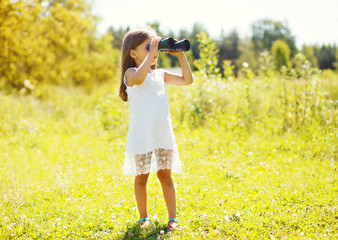 Little girl looks in binoculars outdoors in summer day