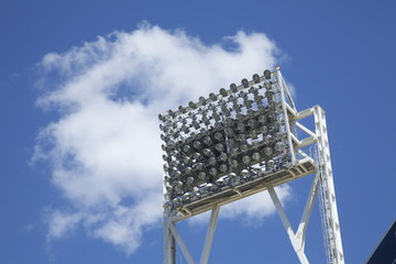 Stadium lights at day against a blue sky and clouds