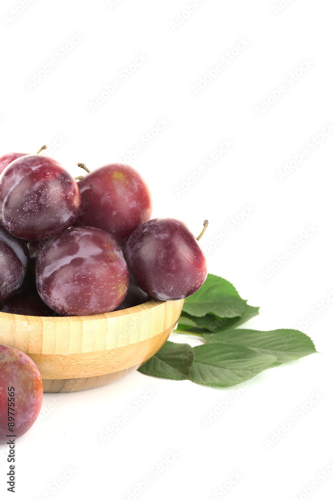 Ripe plums in wooden bowl isolated on white