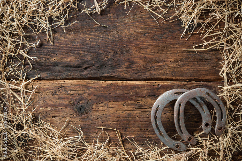 Two old rusty horseshoes with straw on vintage wooden board - obrazy, fototapety, plakaty 