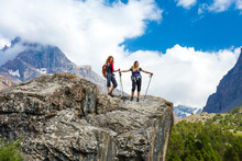 Outdoor Life.
People Walking On Top Of Stone Rock With Trekking Poles And Backpacks Silhouettes On Clouds And Sky Background Mountain Landscape Young Women