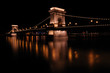 Illuminated Chain Bridge onto a river at night in Budapest