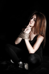 Beautiful young woman with tied arms sitting on the floor