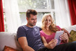 © Joshua Resnick - lovely couple sitting on couch at home watching videos on tablet together