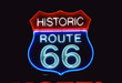 This is a road sign that says Historic Route 66. It is a neon sign in red, white and blue against a black night sky.