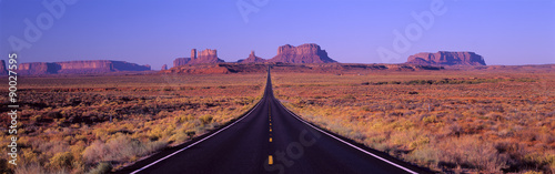 to-jest-trasa-163-ktora-biegnie-przez-rezerwat-indian-navajo-droga-biegnie-w-srodku-i-staje-sie-mniejsza-w-nieskonczonosc-czerwone-skaly-monument-valley-sa-w-tle-szorujace-rosliny-pustyni-sa-po-obu-stronach-drogi