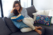 Beautiful young woman reading a book on the sofa.