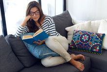 Beautiful Young Woman Reading A Book On The Sofa.