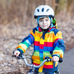 Poster - kid boy in safety helmet and colorful raincoat riding bike, outd