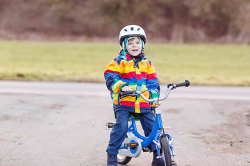 Poster - kid boy in safety helmet and colorful raincoat riding bike, outd