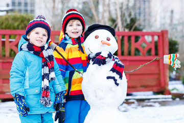 Wall Mural - Two little friends making a snowman, playing and having fun with