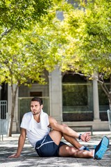 Poster - Handsome athlete with towel stretching his leg on the ground