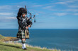 Traditional scottish bagpiper in full dress code with the sea in background