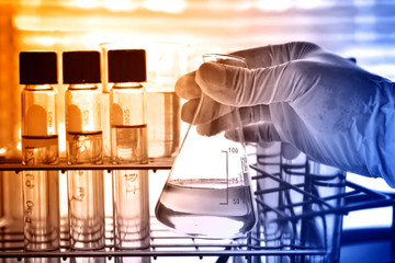 Wall Mural - flask in scientist hand with lab glassware background