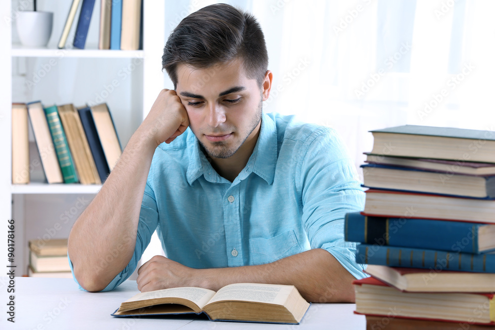 Young man reading book at table in room