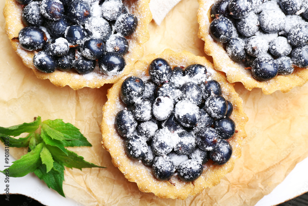 Delicious crispy tarts with black currants on parchment, top view