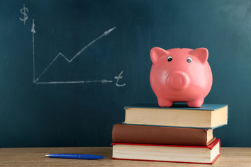 Canvas Print - Piggy bank with books on blackboard background