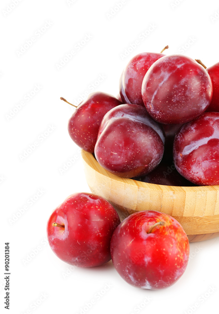 Ripe plums in wooden bowl isolated on white