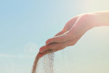 Close-up Of Female Hand Releasing Dropping Sand. Sand Flowing Through The Hands Against Blue Sky. Summer Beach Holiday Vacation Concept. Sun Haze Image