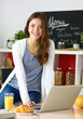 © lenets_tan - Attractive young woman using laptop and sitting in the kitchen