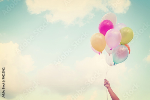 Fotografie, Obraz Girl hand holding multicolored balloons done with a retro vintage instagram filt