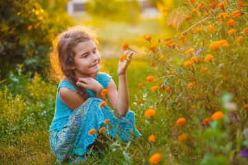 teen girl sitting on his haunches and touching orange flower in 