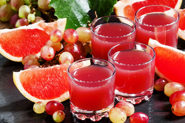 Fresh juice of red grapes and grapefruit on a dark background, s