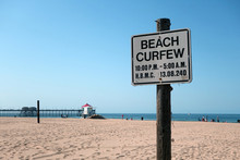 Aged And Worn Vintage Photo Of Beach Curfew Sign With Ocean In Background