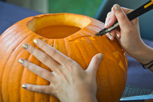 Close Up On The Hands Of A Girl Carving A Halloween Pumpkin