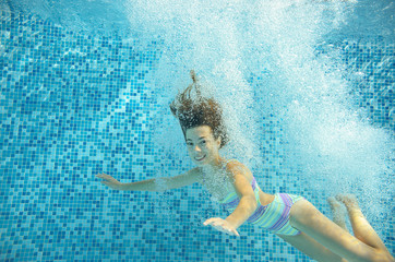 Girl jumps and swims in pool underwater, happy active child has fun in water
