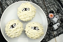 Group Of Halloween Mummy Cupcakes On White Plate With Candies On Black Cloth Background
