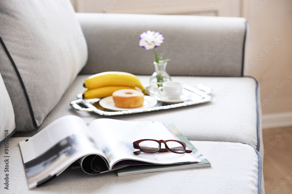 Light breakfast and magazines on sofa in living room, close up