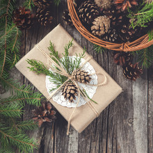 Hand Crafted Gift On Rustic Wooden Background And A Basket With Fir Branches And Cones