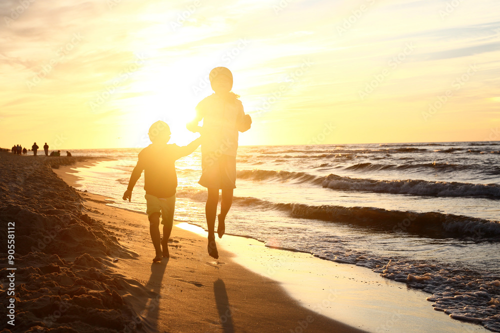 Zabawa przy zachodzie słońca. Dzieci  bawią się na brzegu morza podczas zachodu słońca - obrazy, fototapety, plakaty 
