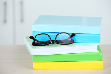 Canvas Print - Stack of books with glasses on wooden table in room, closeup