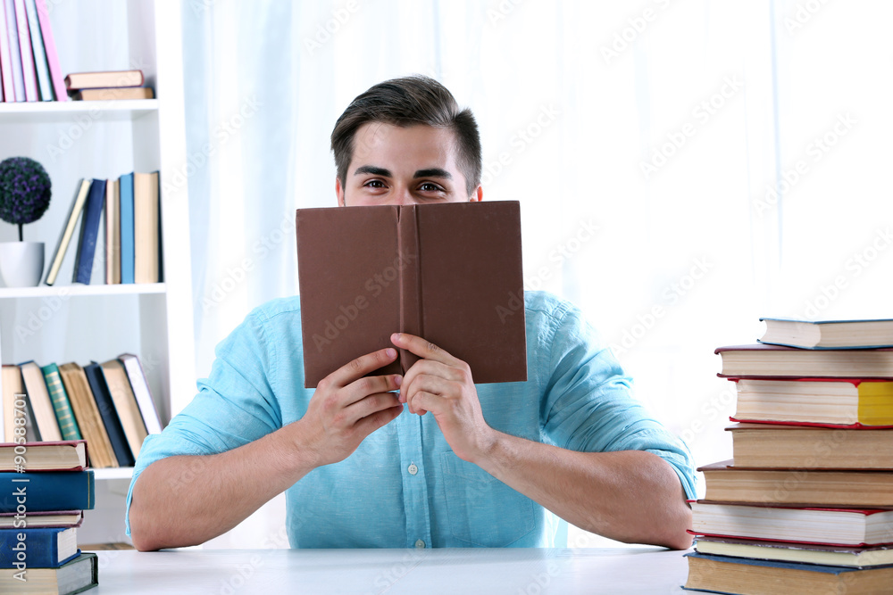 Young man reading book at table in room