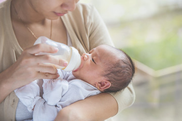 cute newborn baby being fed by her mother using bottle
