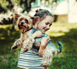 little girl in a striped sweater smiles and holds a small dog