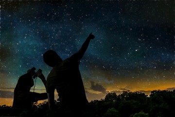 silhouette of adult man observes night sky with child.