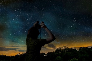Wall Mural - silhouette of adult man is observing stars on night sky with binoculars.