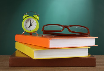 Canvas Print - Stack of books with glasses and alarm clock on desk on green chalkboard background